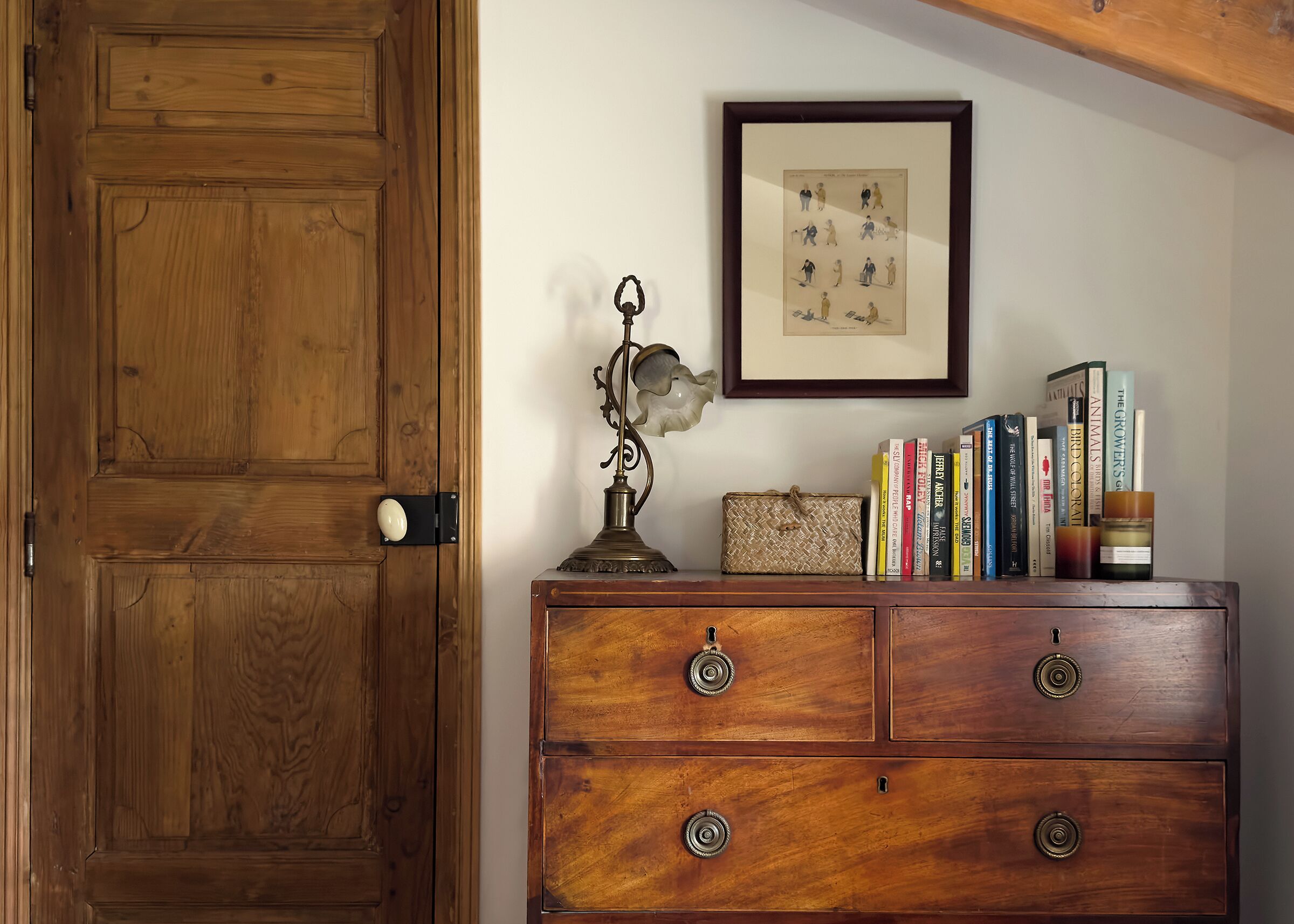 A wooden door, a wooden dresser with drawers, a framed picture, a lamp, and books on the dresser.
