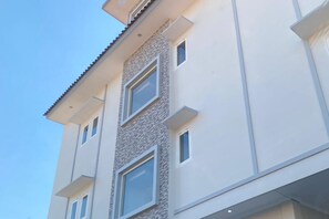 Un edificio de varios pisos con un diseño arquitectónico moderno, que presenta una combinación de superficies de pared lisas y texturizadas, y múltiples ventanas en cada nivel.