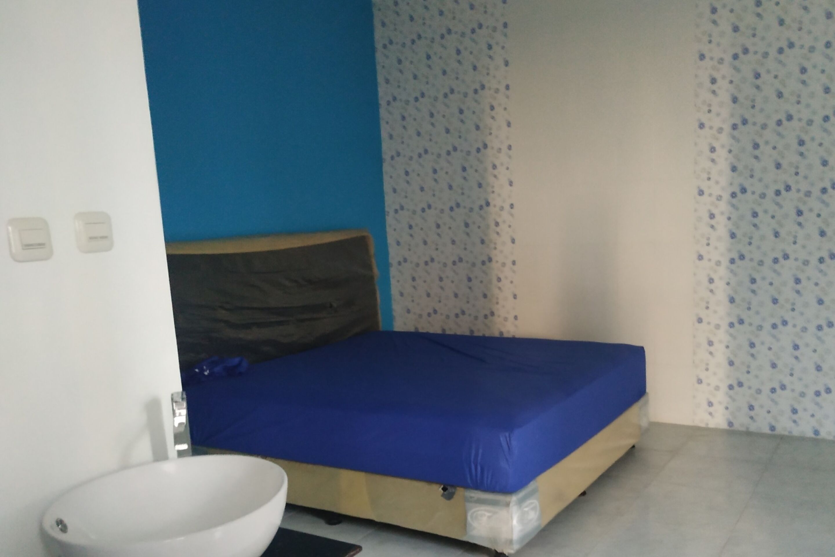 A small room with a single bed, a white sink, and a blue wall.