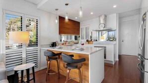 Una cocina moderna con una isla central, taburetes de bar y vistas a través del ventanal.