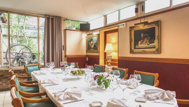 Un comedor con una larga mesa dispuesta para una comida, sillas, un ventanal con cortinas y obras de arte en las paredes.
