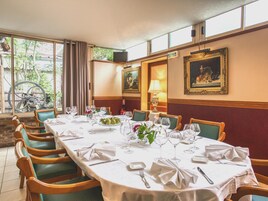 Une salle à manger avec une longue table dressée pour un repas, des chaises, une fenêtre avec des rideaux et des œuvres d’art accrochées aux murs.