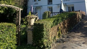 Un edificio de dos pisos con jardín, cerca de madera y pérgola.