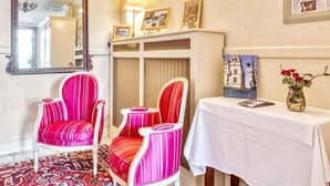 Una habitación con un espejo grande y ornamentado, dos sillas a rayas, una mesa con un florero y un cuadro en la pared.