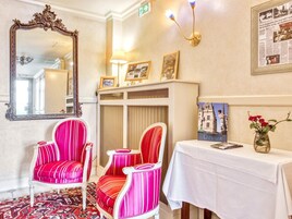 Une pièce comprenant un grand miroir décoratif, deux fauteuils à rayures, une table ornée d’un vase de fleurs et un tableau encadré accroché au mur.