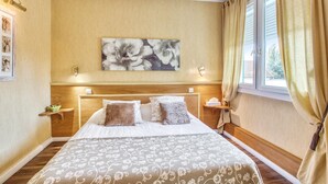 Habitación de hotel con una cama grande, un cabecero de madera, un cuadro floral en la pared y una ventana con cortinas.