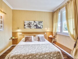 Une chambre d’hôtel avec un grand lit, une tête de lit en bois, un tableau floral accroché au mur et une fenêtre avec des rideaux.