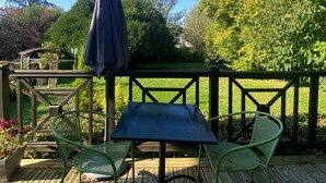 Una terraza de madera con una mesa y dos sillas, rodeada por un cerco de madera y abundante vegetación.
