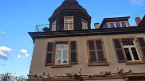 Ein Gebäude mit einem markanten Turm, zahlreichen Fenstern mit Fensterläden und einem strahlend blauen Himmel im Hintergrund.
