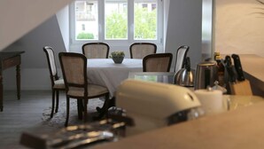 Ein Essbereich mit Tisch für vier Personen, Stühlen, einer Topfpflanze und Küchenutensilien auf der Arbeitsfläche.