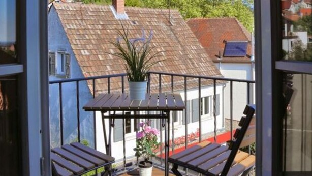Ein Balkon mit Holzterrasse, zwei Klappstühlen, einem kleinen Tisch und einem Blumentopf.