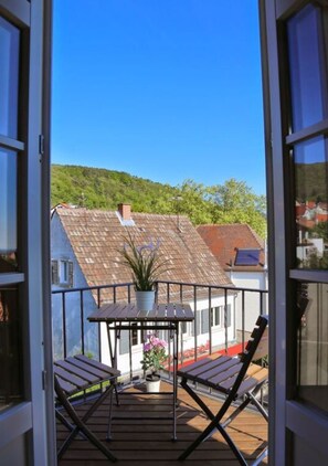 Un balcon doté d’une terrasse en bois, de deux chaises pliantes, d’une petite table et d’une plante en pot.