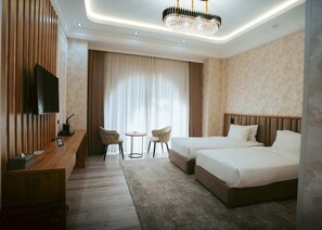 A hotel room with a wooden desk, two chairs, a bed, a TV, and a chandelier. - Baden-Baden Hotel (Tashkent)