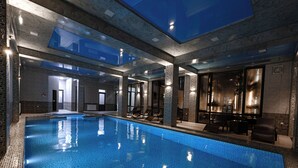 A large indoor swimming pool with clear blue water, surrounded by stone walls and modern furnishings. - Baden-Baden Hotel (Tashkent)