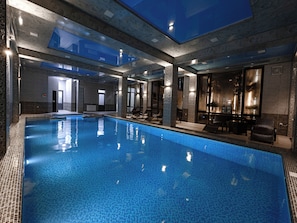 A large indoor swimming pool with clear blue water, surrounded by stone walls and modern furnishings. - Baden-Baden Hotel (Tashkent)