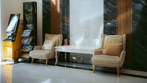 A lobby with two leather armchairs, a reception desk, a digital kiosk, and a marble wall. - Baden-Baden Hotel (Tashkent)