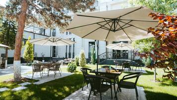 An outdoor patio area with tables and chairs, umbrellas, and a building in the background.