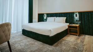 A hotel room with a large bed, a bedside table, a chair, and a view of the outdoors. - Baden-Baden Hotel (Tashkent)
