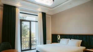 A hotel room with a large bed, a chair, a nightstand, and a view of the outdoors through a sliding door. - Baden-Baden Hotel (Tashkent)