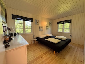 A room with a bed, a small table, a lamp, and two windows with blinds.