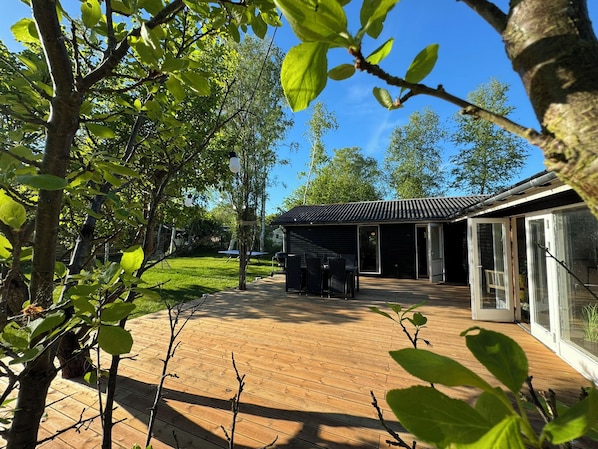 A wooden deck with a covered outdoor seating area, a building with a metal roof, and a glass door leading to a patio.