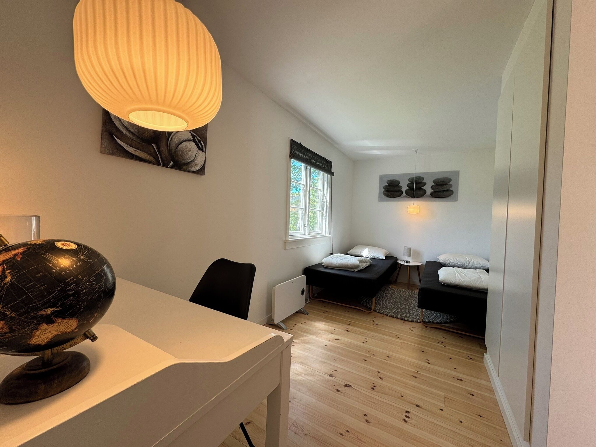 A compact room with a globe on a desk, a bed with a pillow, a small table, and a window with a view.