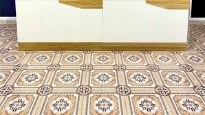 Un canapé blanc agrémenté de détails en bois, dans une pièce dont le sol est recouvert de carreaux décoratifs et une des murs est de couleur unie.