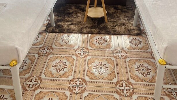 Une chambre d’hôtel avec deux lits, un canapé, une petite table ronde ornée d’une plante et un carrelage au motif décoratif.