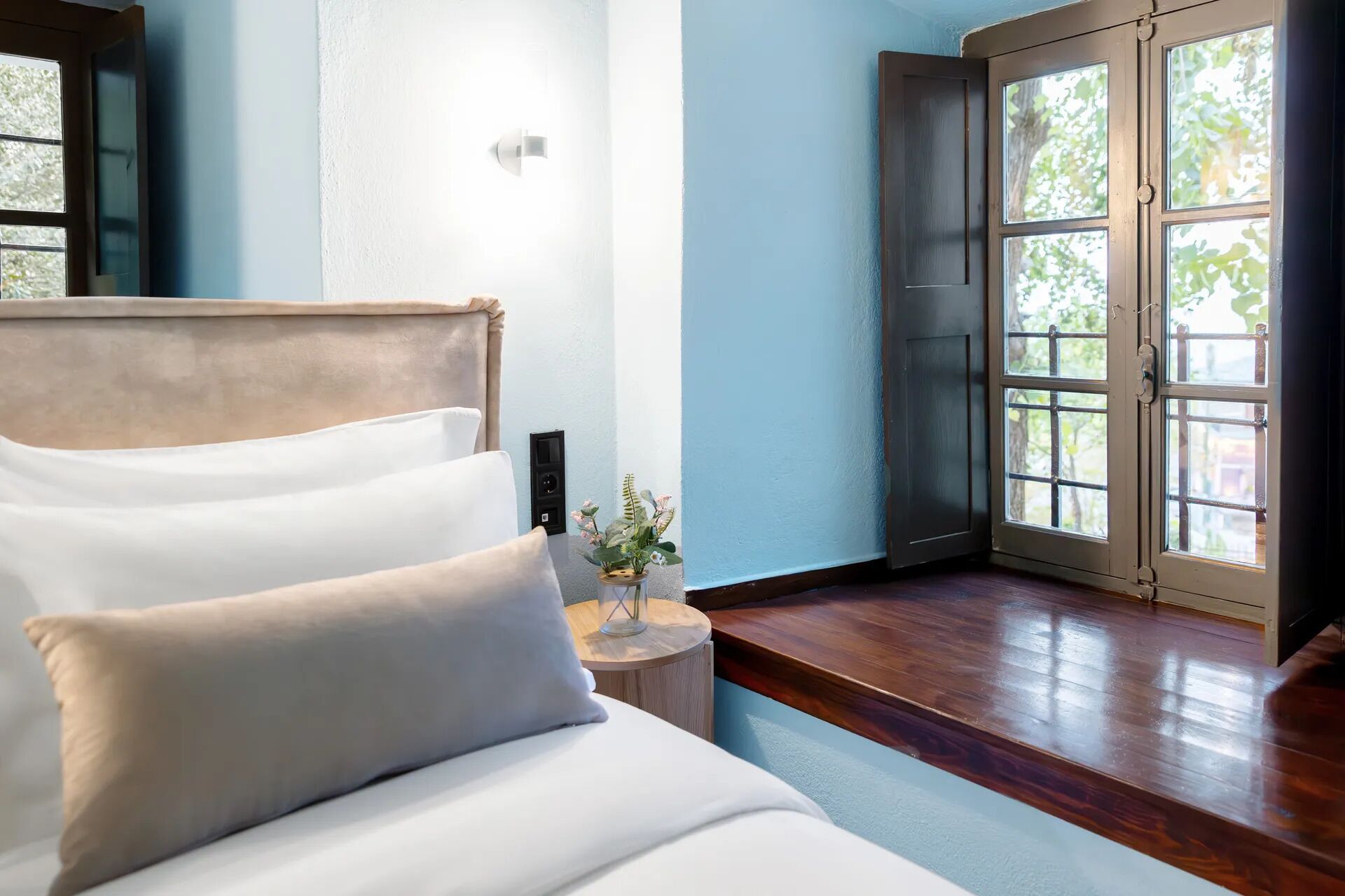 Un dormitorio con una cama, una mesita de noche con un florero y una puerta que da a un balcón.