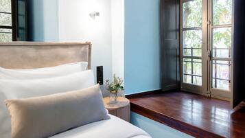 Un dormitorio con una cama, una mesita de noche con un florero y una puerta que da a un balcón.