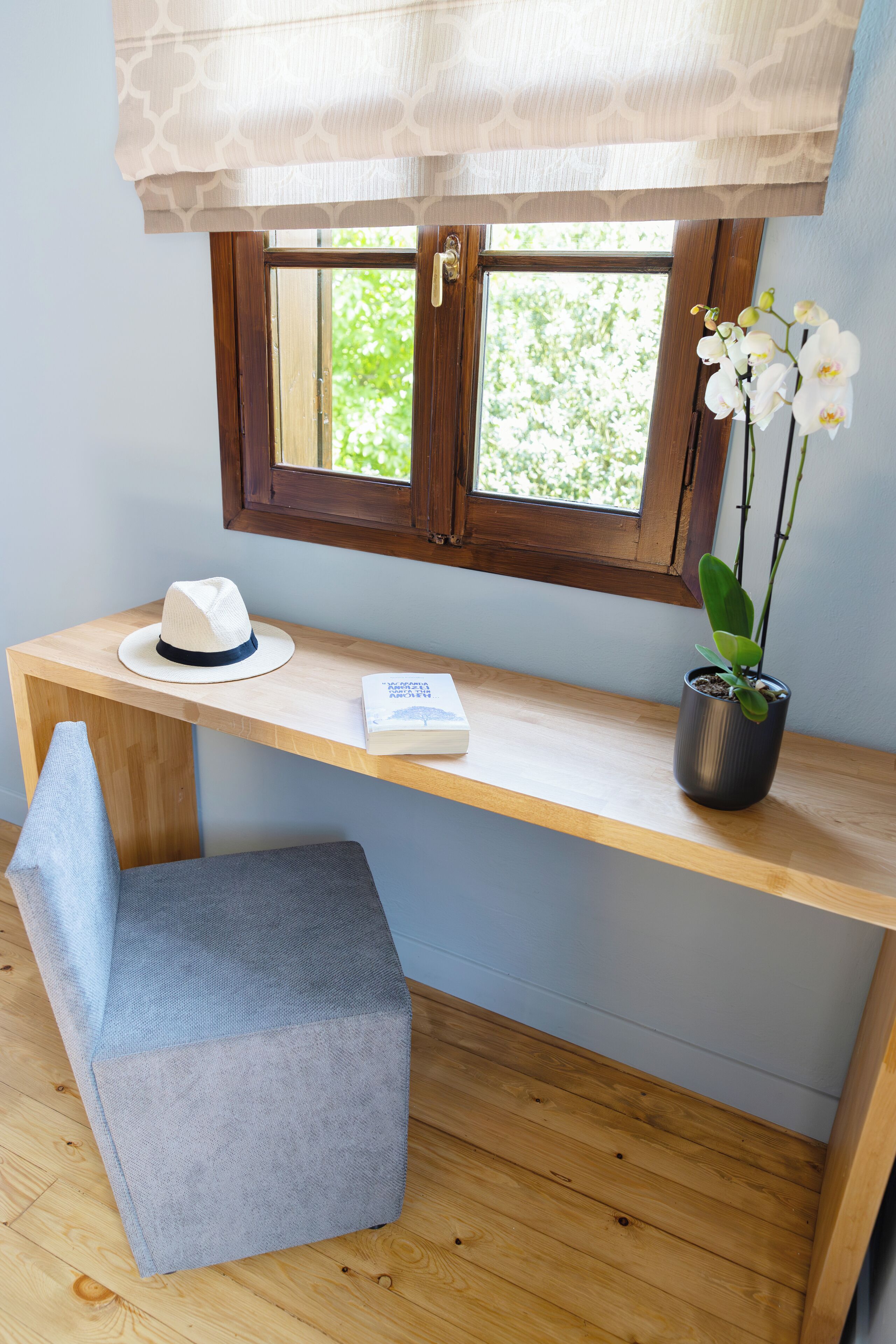 Un bureau en bois sur lequel se trouvent un chapeau blanc, un livre et une orchidée en pot.