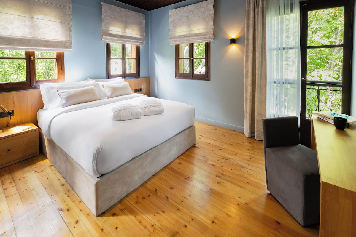 A bedroom with a large bed, wooden flooring, and a desk with a chair.