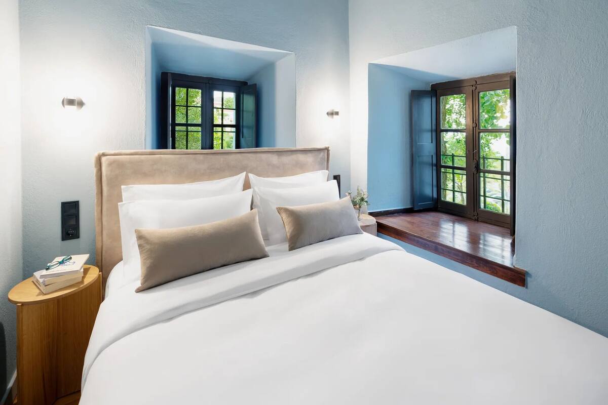 A bedroom with a large bed, two windows, and a nightstand.
