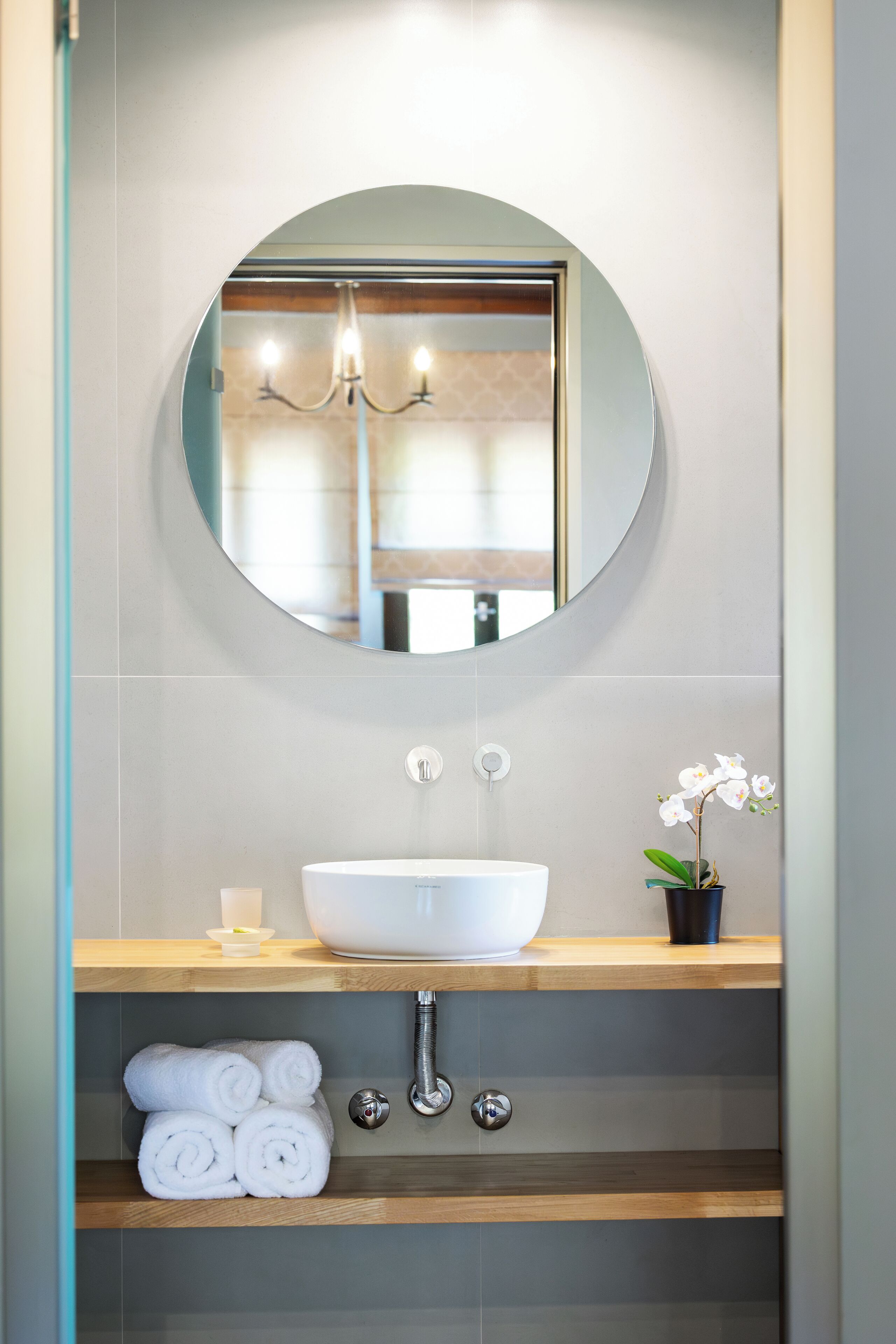 A bathroom with a round mirror, white sink, and a potted orchid.