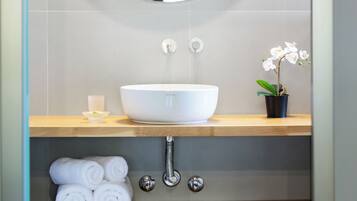 A bathroom with a round mirror, white sink, and a potted orchid.