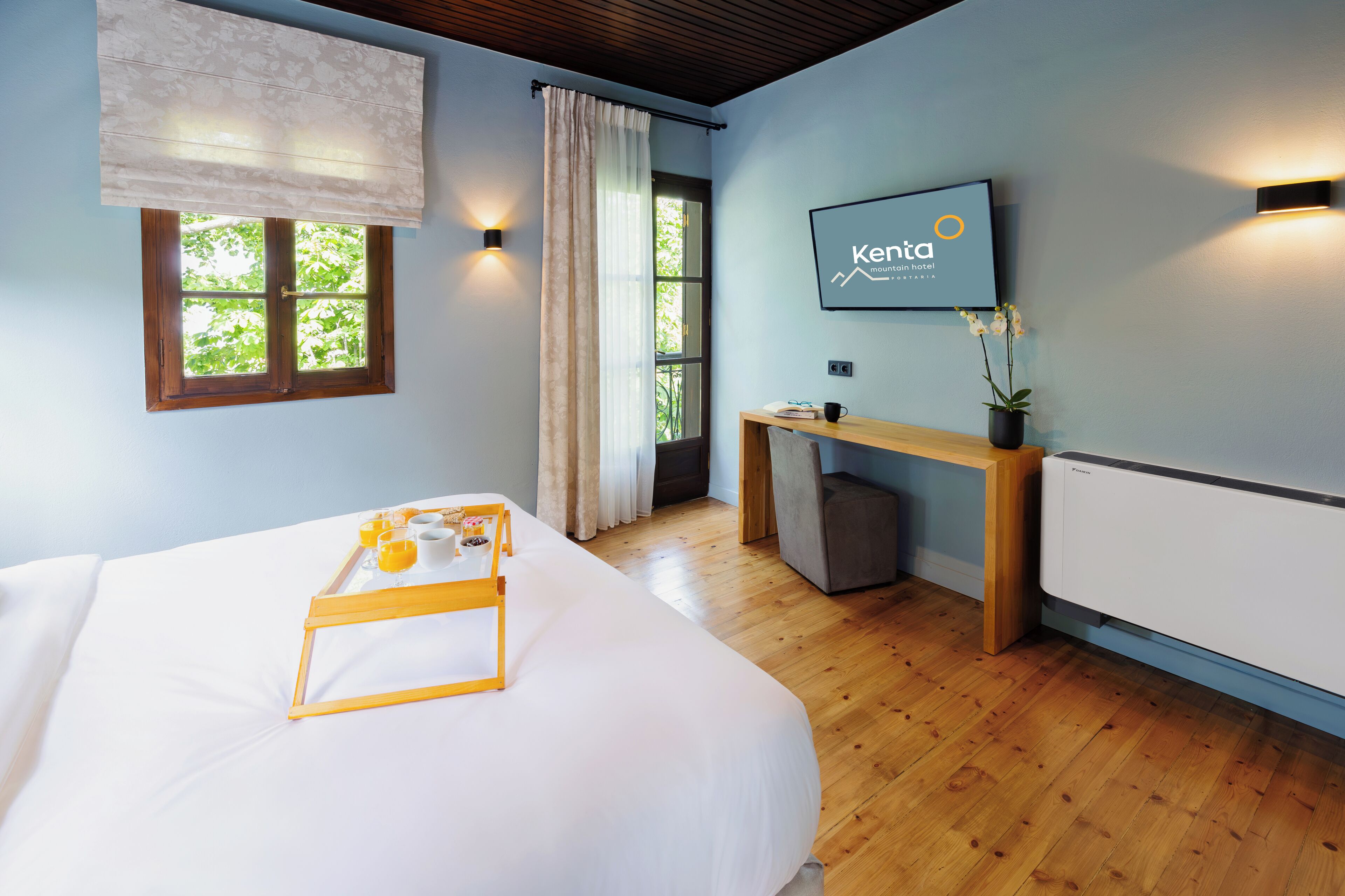 Ein Hotelzimmer mit Bett, Schreibtisch, Stuhl, einem Fenster mit Vorhängen, einem an der Wand befestigten Fernseher und einer Heizung.