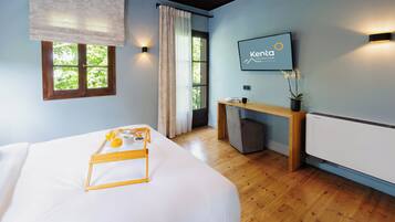 Ein Hotelzimmer mit Bett, Schreibtisch, Stuhl, einem Fenster mit Vorhängen, einem an der Wand befestigten Fernseher und einer Heizung.