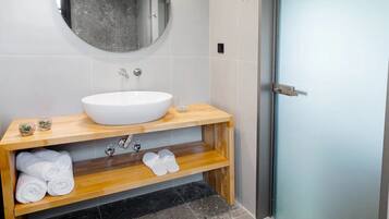 A modern bathroom with a white sink, wooden vanity, a round mirror, and a glass door.