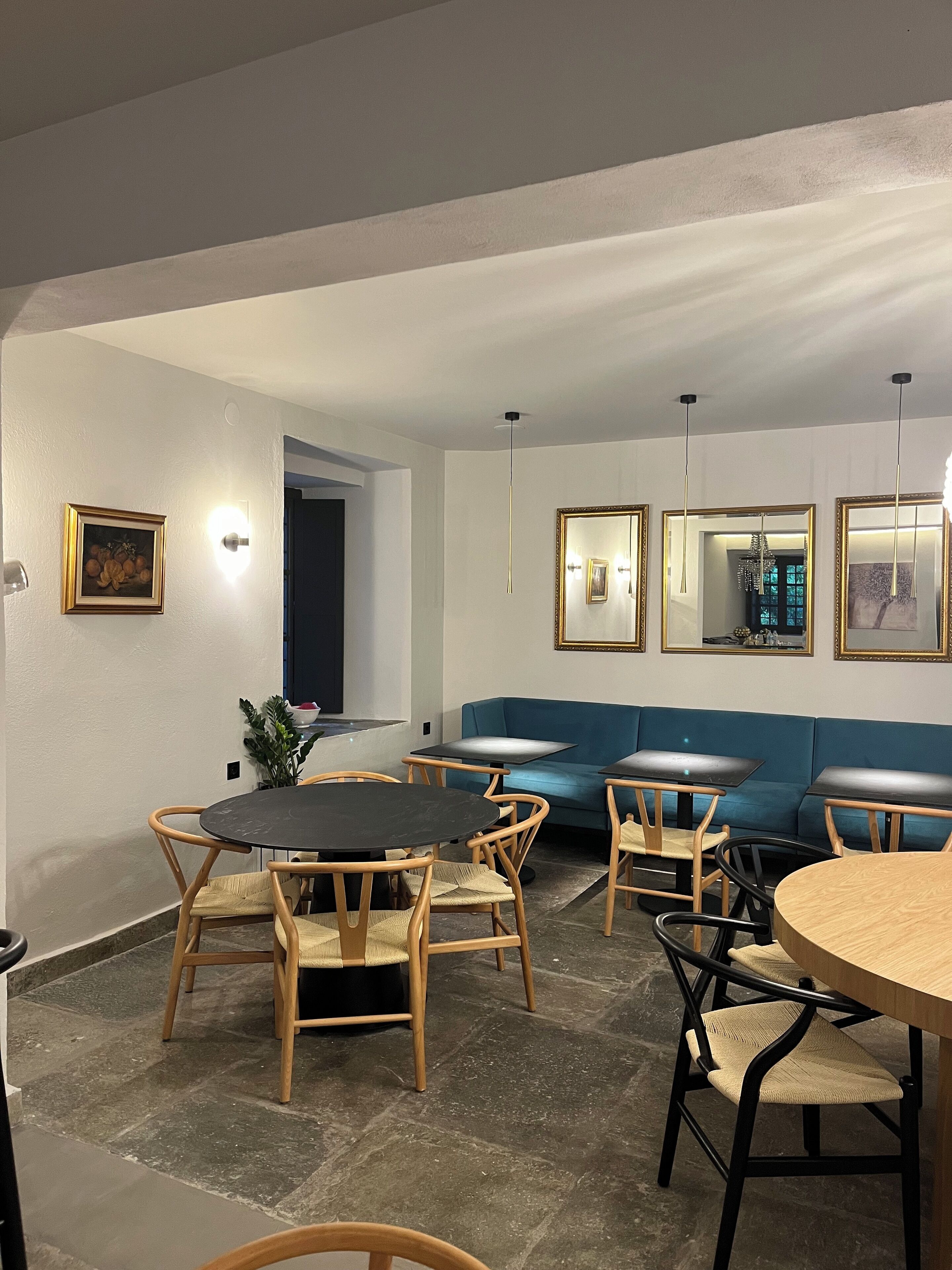 Un interior moderno con comedor que incluye mesas y sillas redondas, un sofá azul y espejos en la pared.