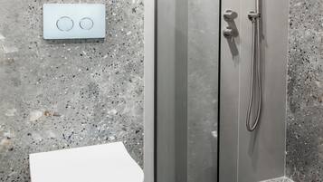 Un baño moderno con inodoro blanco, cabina de ducha de vidrio y suelo de losas de granito.