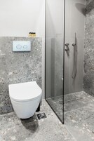 Un baño moderno con inodoro blanco, cabina de ducha de vidrio y suelo de losas de granito.