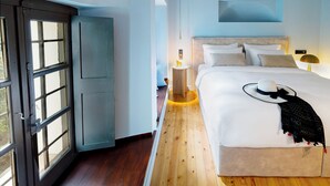 A bedroom with a large bed, a nightstand with a lamp, and a view through an open door. - Kenta Mountain Hotel (Volos)