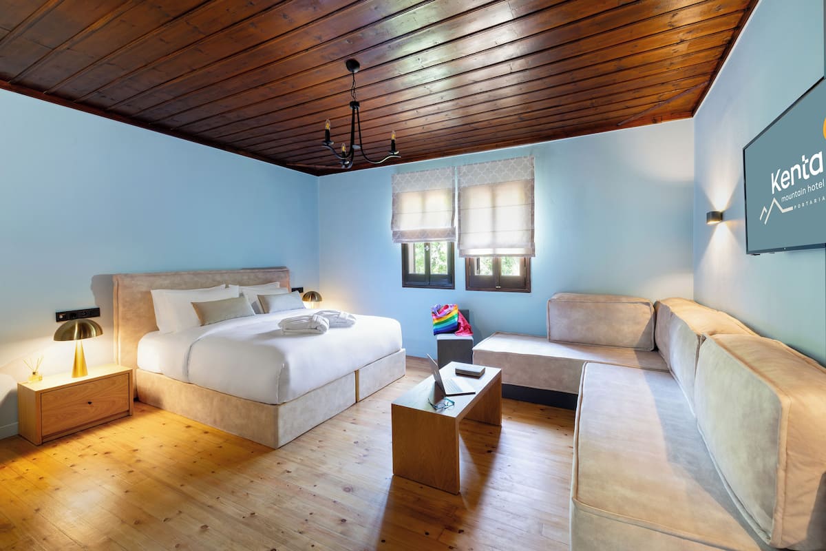 A modern hotel room with a wooden ceiling, a large bed, a sofa, and a small table.
