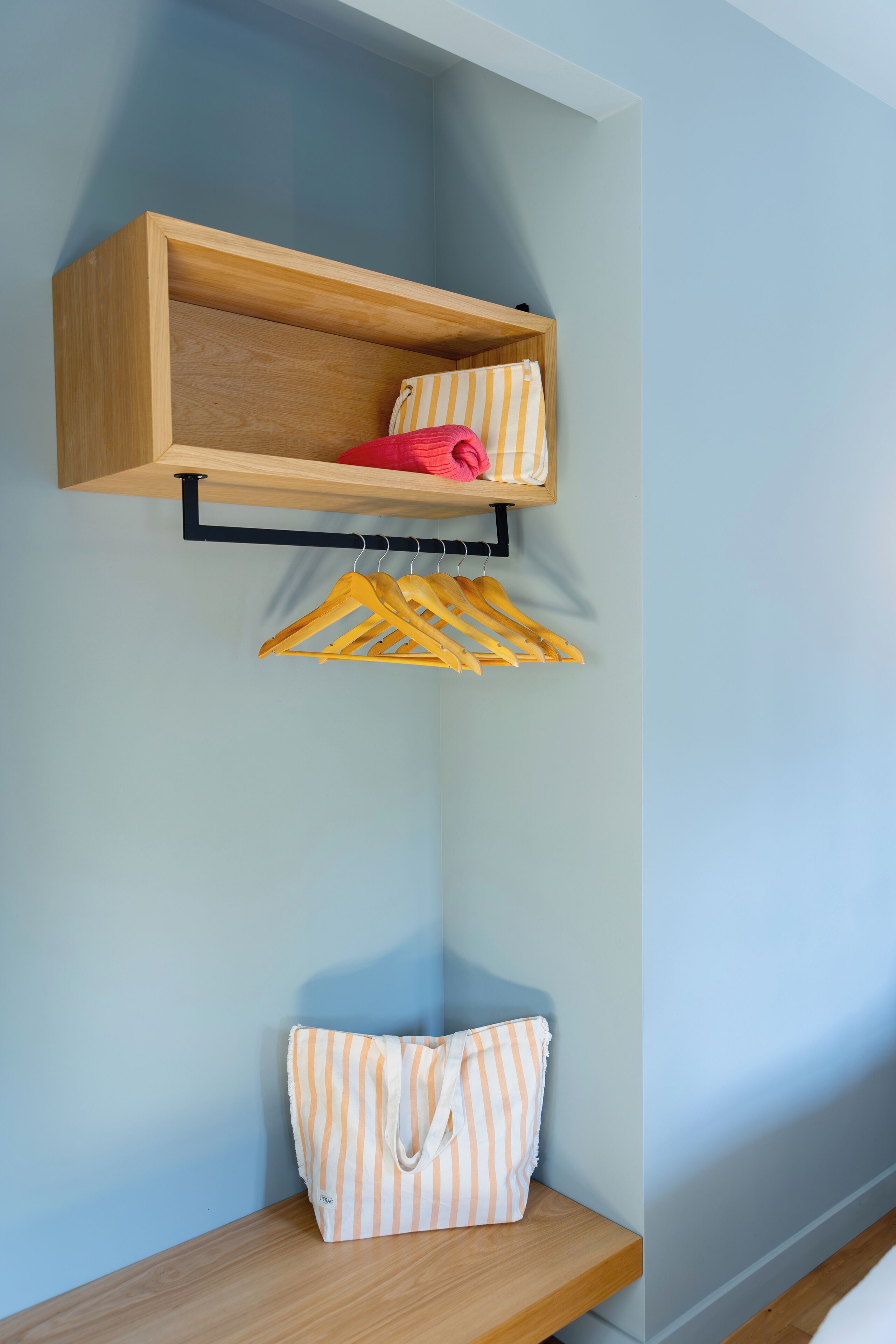 A corner with a wooden shelf holding a striped bag and a red item, and a wooden bench below.
