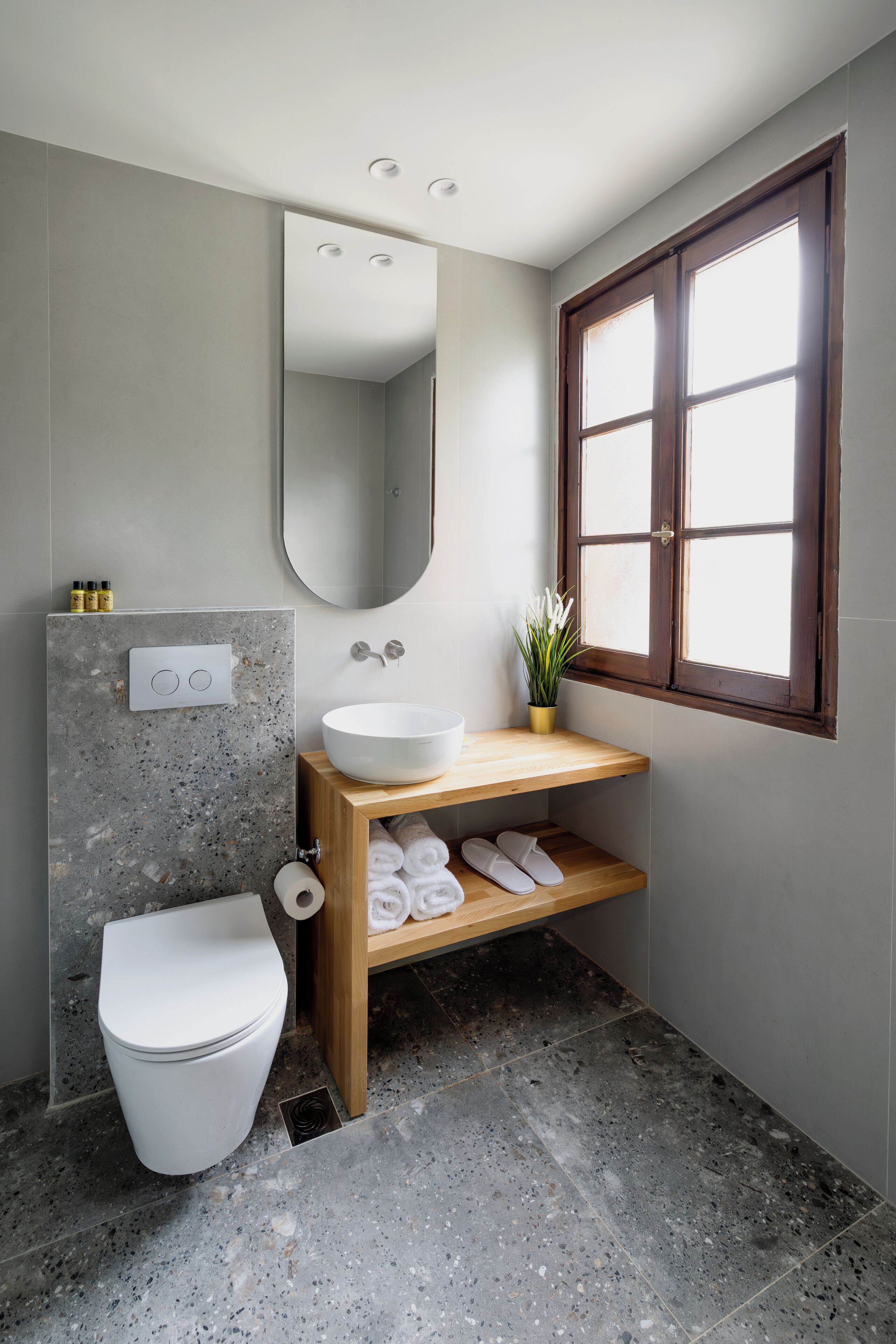 A modern bathroom with a white toilet, a wooden vanity with a sink, a mirror, and a window with wooden frames.