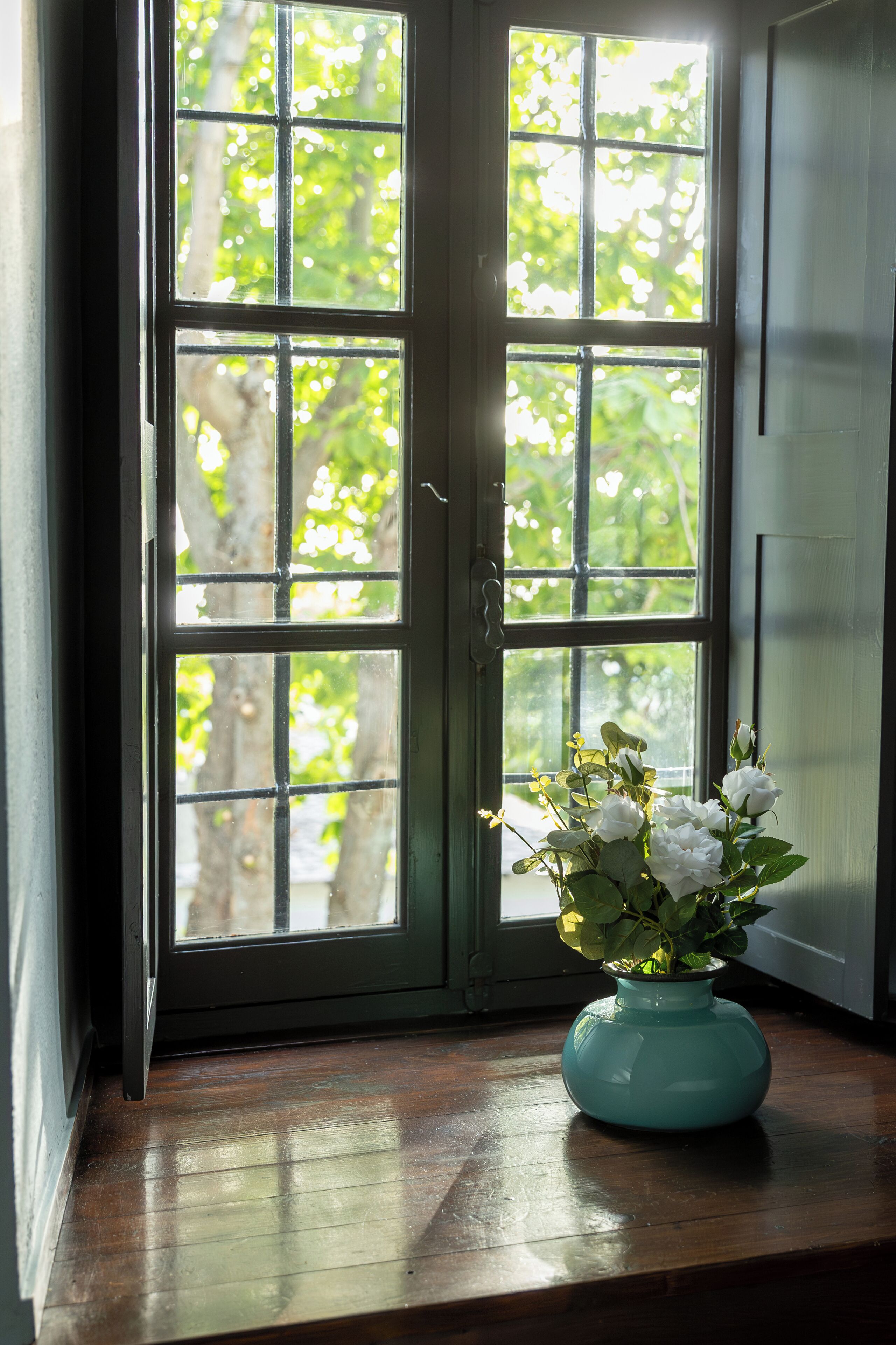 A window with a view of trees, a teal vase with flowers on a wooden ledge.