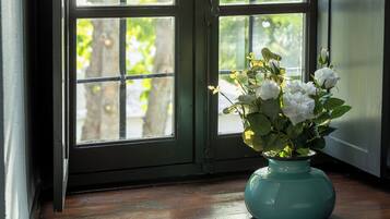 Ein Fenster mit Blick auf Bäume, eine türkisblaue Vase mit Blumen auf einem Holzboden.
