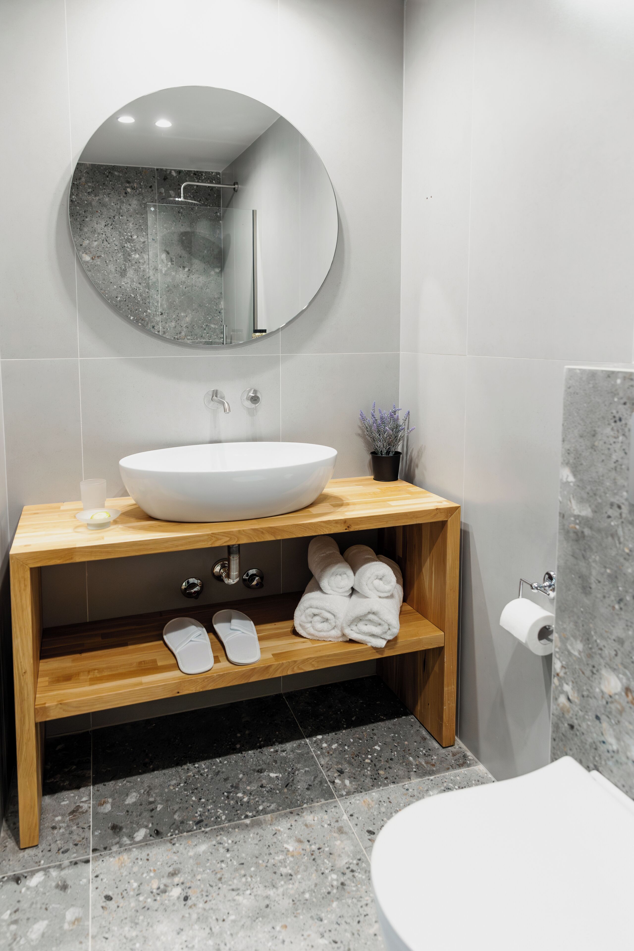 A modern bathroom with a round mirror, a white sink, and a wooden vanity.