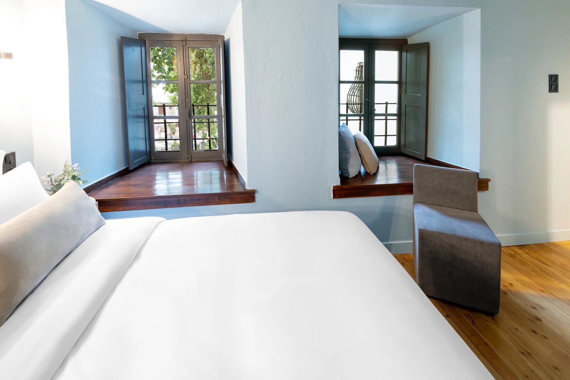 A modern bedroom with a large bed, a window seat with a chair, and a view of the outdoors.