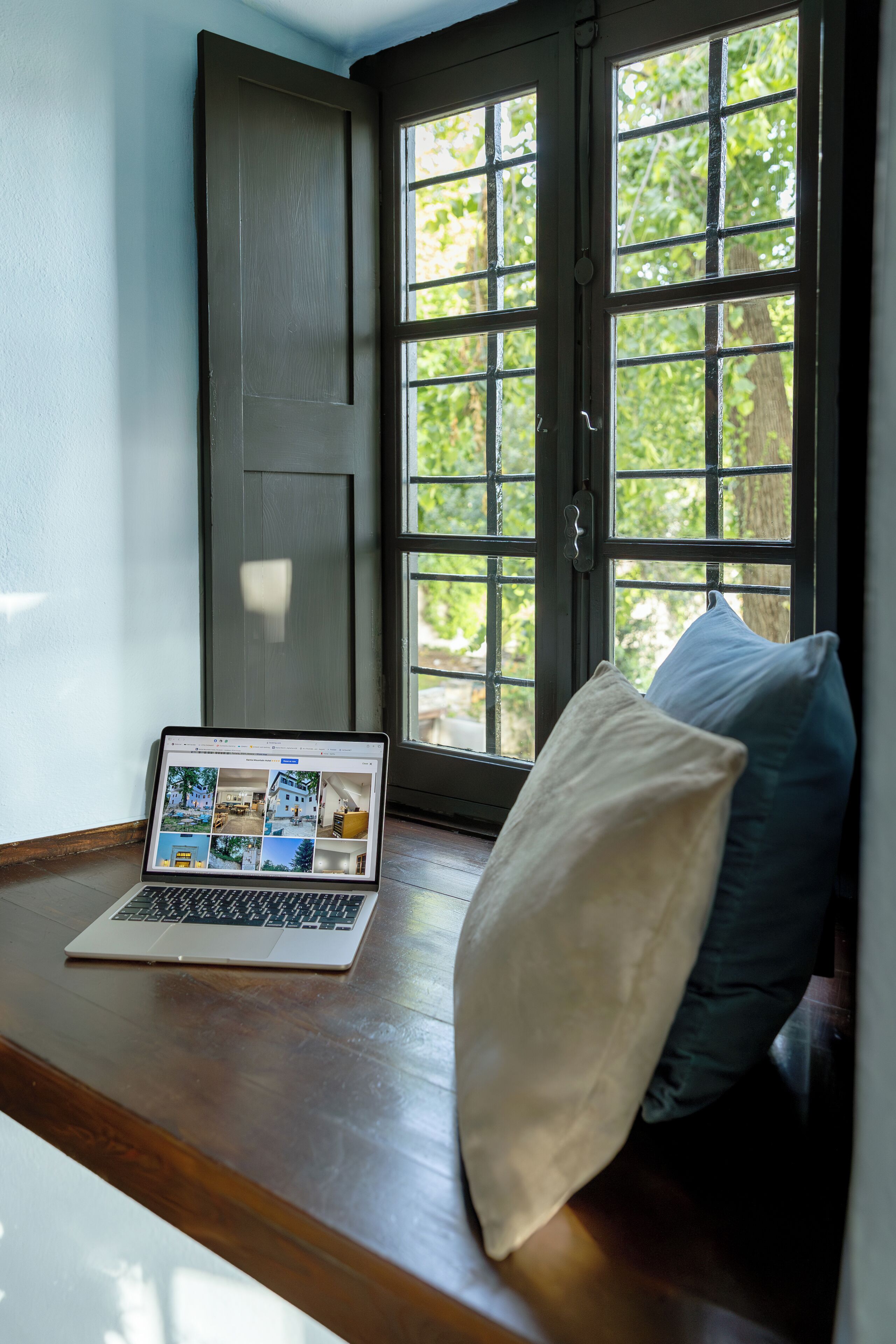Una computadora portátil sobre un banco de madera junto a una ventana con vista a follaje.